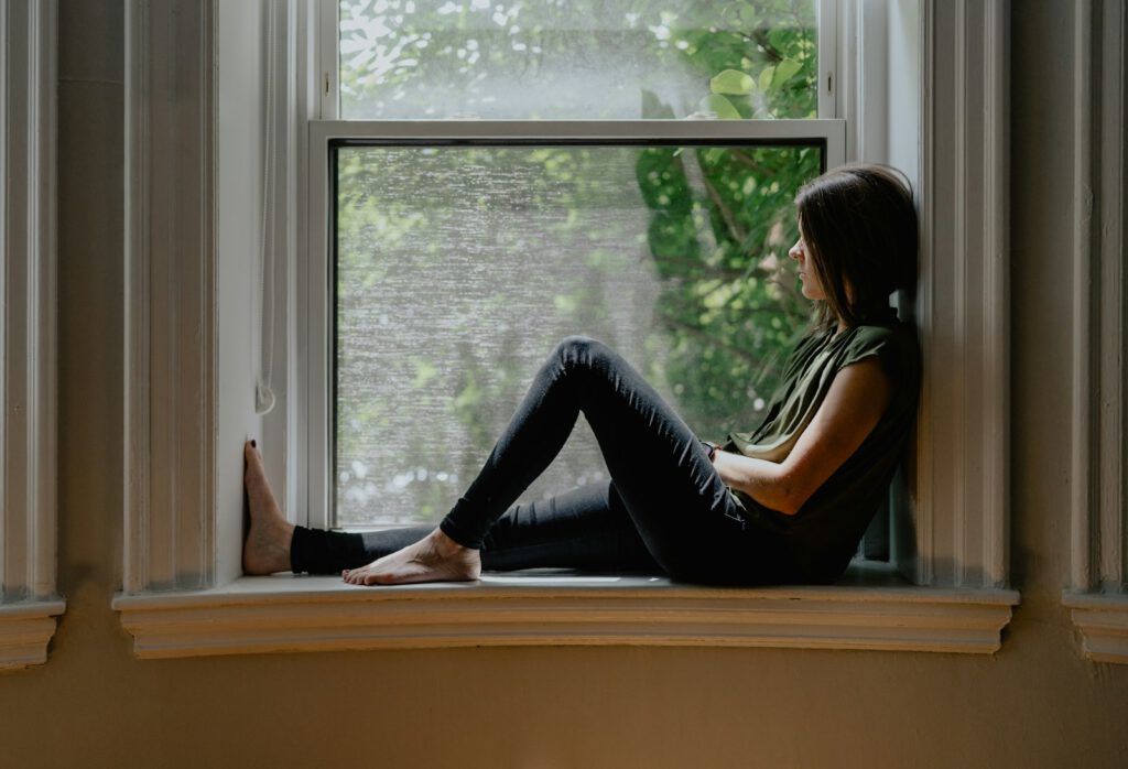 Frau sitzt nachdenklich auf einer Fensterbank