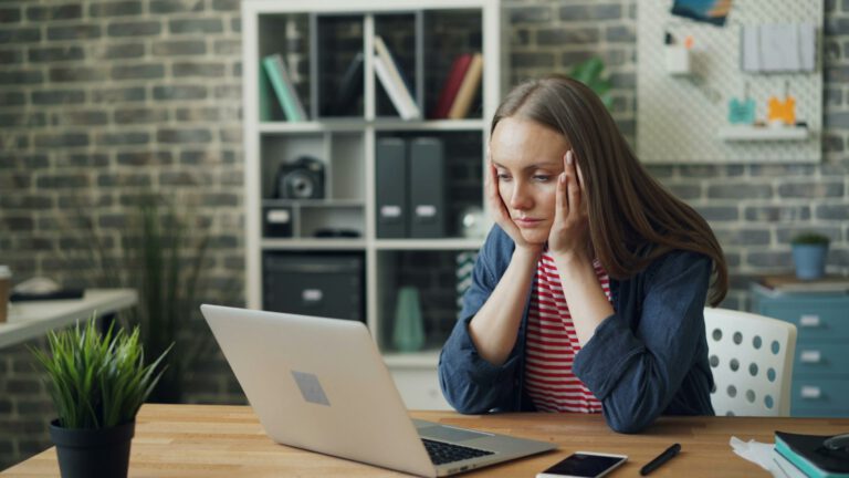 Frau sitzt nachdenklich am Tisch vor ihrem Laptop