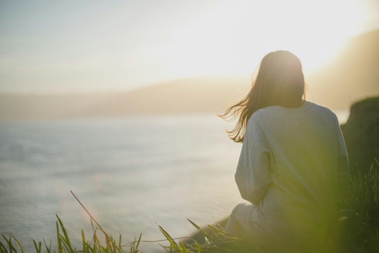 Frau steht ruhig am Meer und blickt auf das Wasser